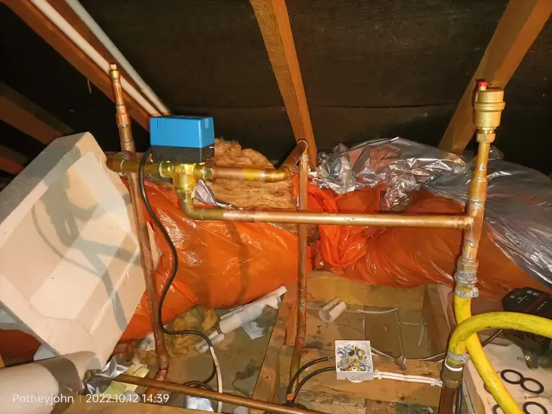 Central heating pipework and motorised zone valve in a loft, part of a heating system being flushed near Crediton
