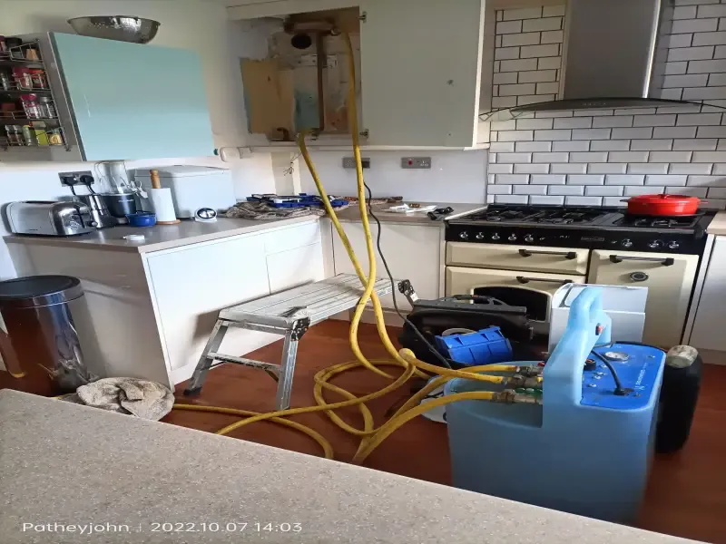 Power flushing machine connected to a central heating system in a mid Devon kitchen, hoses running to the boiler